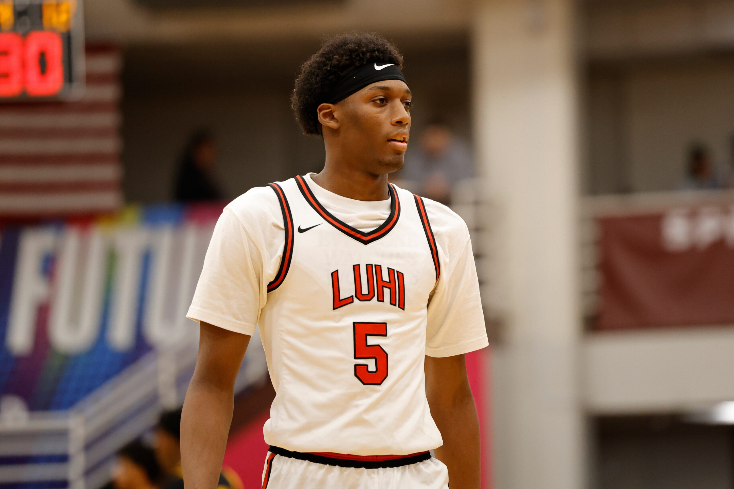 A basketball player in a white jersey with red trim and the number 5, wearing a black headband, looking to the right.